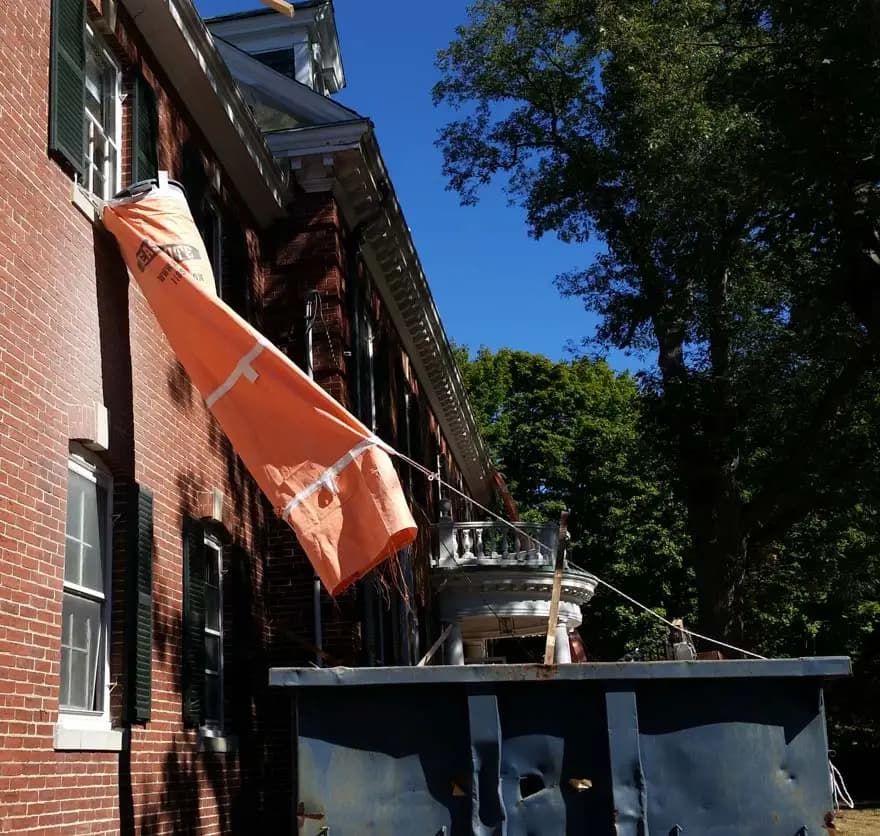 EasyChute angled from a brick building window into a roll-off dumpster on a New Britain CT job site